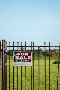 A large plot of land bordered by an iron fence, complete with a 'For Sale' sign in Miami, FL. Ideal for development.
