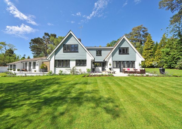 Modern family home exterior showcasing a large lawn and garden under a clear blue sky.
